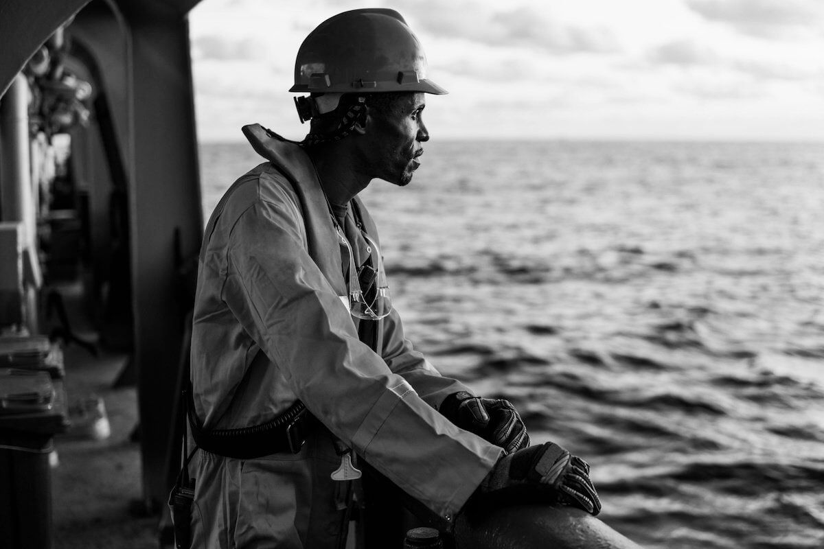 Seafarer in a hard hat and lifejacket looking out to sea from a ship's rail